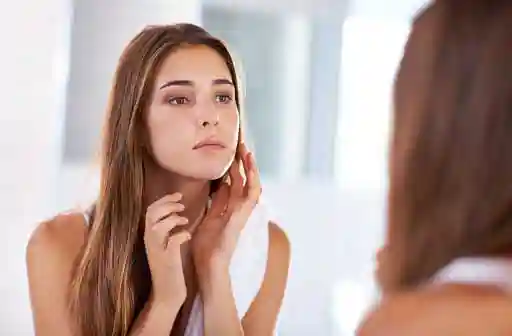 young beautiful woman looking at her face with concern